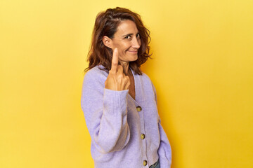 Middle-aged woman on a yellow backdrop pointing with finger at you as if inviting come closer.