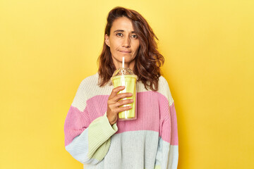 Woman sipping vanilla shake on yellow backdrop