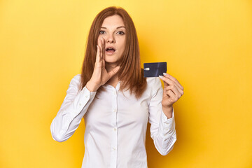 Redhead holding credit card, financial concept shouting and holding palm near opened mouth.