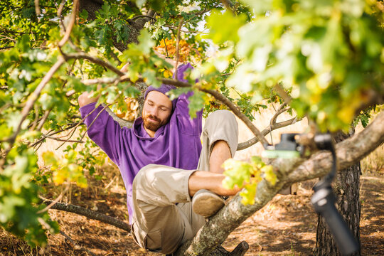 Young beaytiful guy laying lazy on the tree brunch in purple clothes