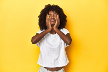 Teen girl in white tank top, yellow studio background crying, unhappy with something, agony and...