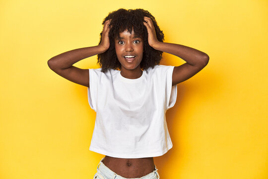 Teen girl in white tank top, yellow studio background screaming, very excited, passionate, satisfied with something.
