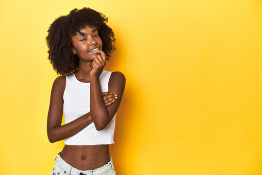 Teen girl in white tank top, yellow studio background relaxed thinking about something looking at a copy space.