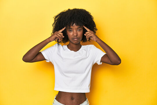 Teen girl in classic white T-shirt, yellow studio backdrop focused on a task, keeping forefingers pointing head.
