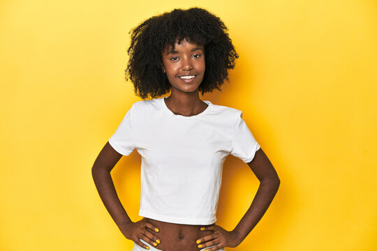 Teen girl in classic white T-shirt, yellow studio backdrop confident keeping hands on hips.