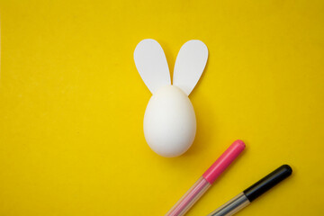 Food photo. Happy Easter. Chicken egg with rabbit ears and pink and black felt-tip pens on yellow...