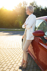Businesswoman wearing white official style suit near her red automobile on parking