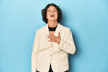 Young woman in elegant white blazer laughs out loudly keeping hand on chest.