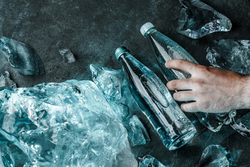 Man hand holding bottle of water in ice. Pieces ice illuminated with blue light. Advertising...