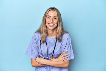 Young caucasian nurse in blue studio laughing and having fun.