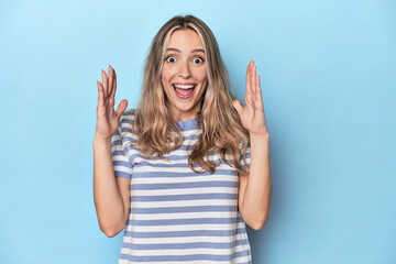 Fototapeta premium Blonde young caucasian woman in blue studio celebrating a victory or success, he is surprised and shocked.