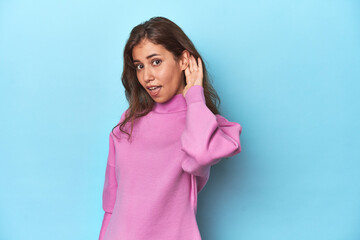 Teen girl in cozy pink sweatshirt on blue trying to listening a gossip.