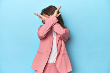 Teen girl in chic pink suit on a blue background keeping two arms crossed, denial concept.