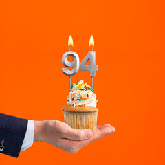 Hand holding birthday cupcake with number 94 candle - background orange