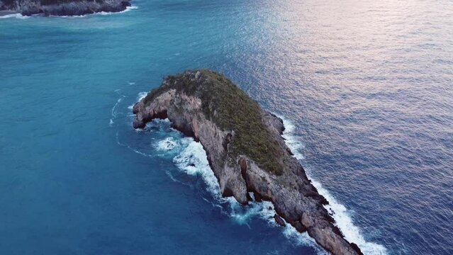 This footage aws made with a drone, at the end of the day, at sunset, with a uninhabited island as the main object, and the beach with trees at the background