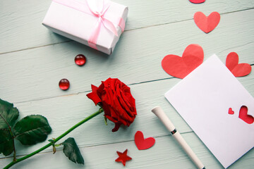 Love composition - red rose, gift box and greeting card on wooden background, top view. Wedding or...