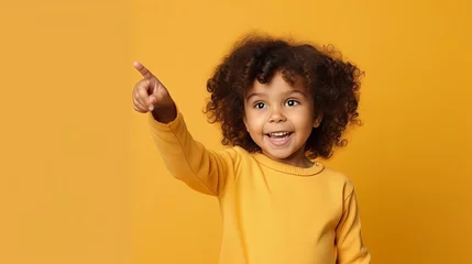 Foto op Canvas Portrait, studio and happy child pointing hand at space with a smile on face on yellow background. Young girl kid with happiness, carefree and positive attitude to show product placement mockup deal © chanidapa