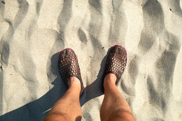 Men with beach shoes stand on sunny sandy beach. Personal perspective used. space for text.