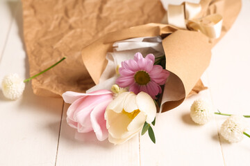 Mini bouquet of beautiful spring flowers in wrapping paper on white wooden background, closeup. International Women's Day