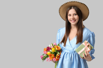 Beautiful young pregnant woman with bouquet of tulips and gift box on grey background. International Women's Day