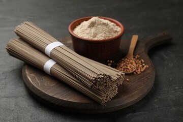 Uncooked buckwheat noodles (soba), flour and grains on black table