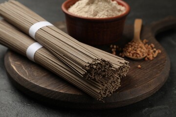 Uncooked buckwheat noodles (soba), flour and grains on black table, closeup