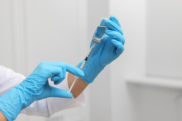 Doctor filling syringe with medication from glass vial indoors, closeup