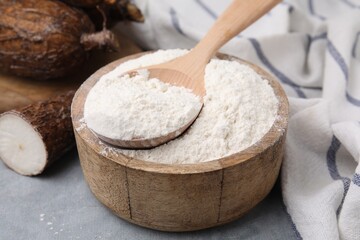 Fototapeta na wymiar Wooden bowl and spoon with cassava flour on grey table, closeup