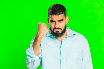 Aggressive angry Indian young man trying to fight at camera, shaking fist, boxing with expression, punishment, threaten, bullying, abuse, mad fury. Arabian guy isolated on green chroma key background