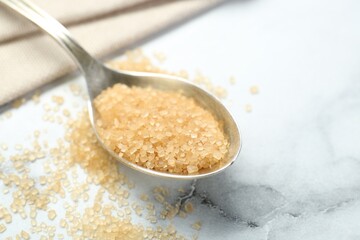 Spoon with brown sugar on white marble table, closeup. Space for text