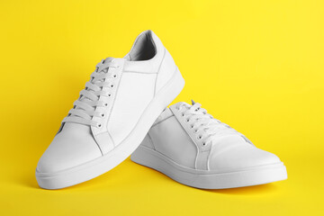 Pair of stylish white sneakers on yellow background