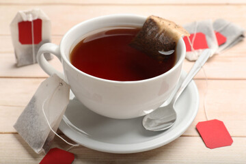 Tea bags, cup of hot beverage and spoon on light wooden table, closeup