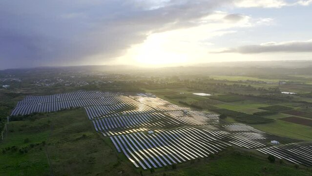 Solar energy farm in with massive array of solar panels with dramatic sky and sun shining. Aerial HDR ProRes drone footage flyover.