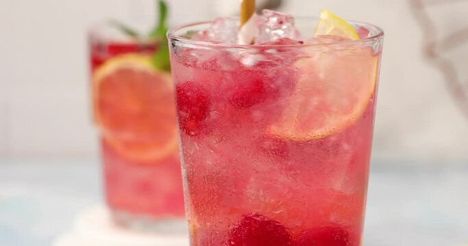 Raspberry lemonade or cocktail with slices of lemon and fresh mint being stirred with a straw