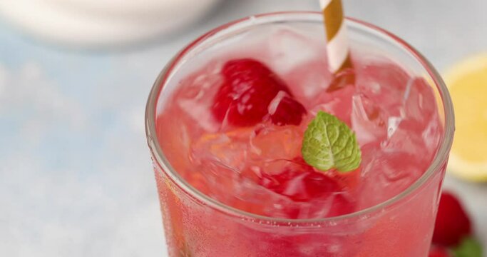 Raspberry lemonade or cocktail with slices of lemon and fresh mint being stirred with a straw