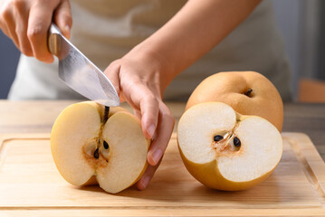 Asian pear fruit or Nashi pear with hand holding kitchen knife and cutting on wooden board