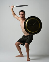 Full length portrait of fit handsome shirtless asian male model,  Holding sword weapon and Spartan shield,  standing in warrior training action pose, isolated on white studio background.