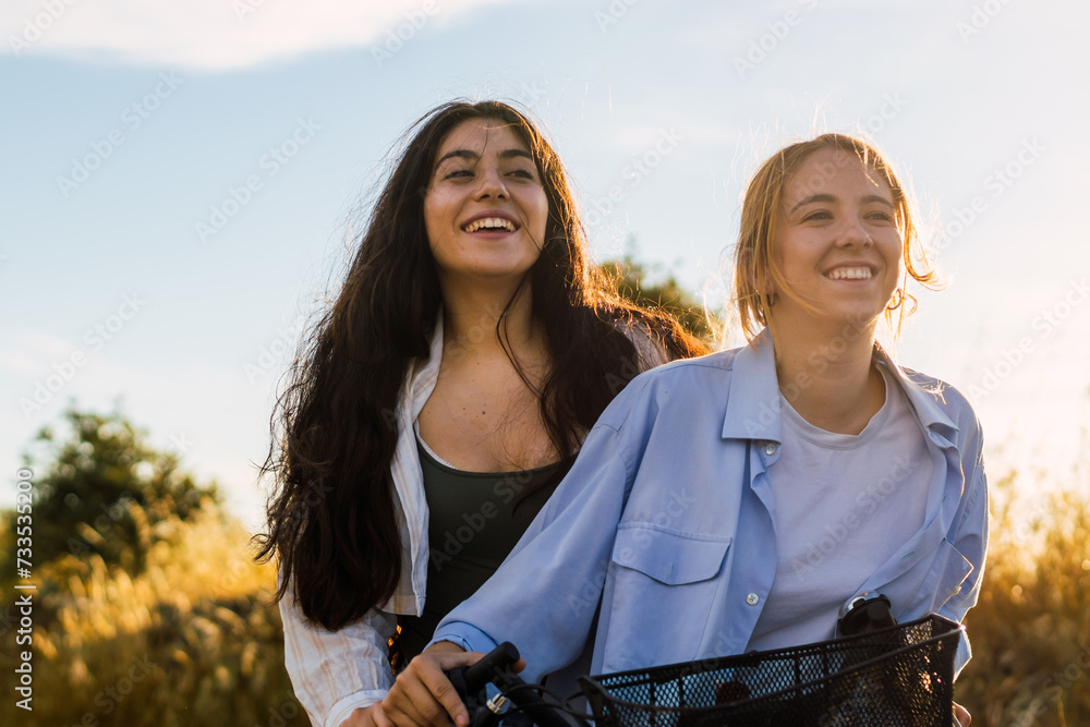 Wall mural two young women on a bike in a field at sunset