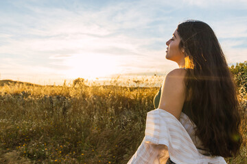 attractive brunette woman portrait on a field during sunset. side view