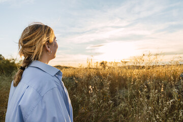 back view of a beauty blonde woman portrait on a field during sunset