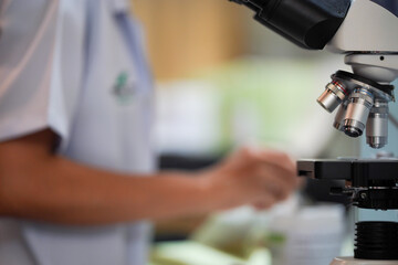 A microscope in a laboratory with blurred of laboratory staff recording details from viewing the sample under a microscope.