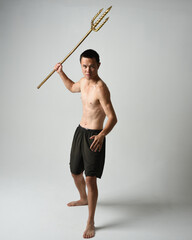 Full length portrait of fit handsome shirtless asian male model,  Holding golden trident weapon,...