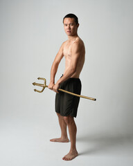 Full length portrait of fit handsome shirtless asian male model,  Holding golden trident weapon,...