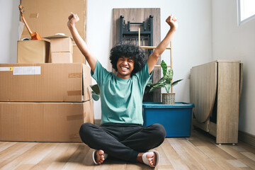 Happy Asian young man raising hands. celebrating move to new house while sitting on the floor