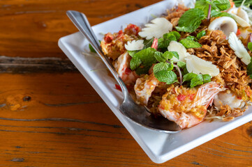 Close up of spicy Thai shrimp salad serving on wooden table.