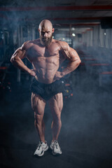 Muscular bald man posing in shorts. Bodybuilder showing off his shape in the gym. 