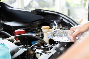 A woman refilling the radiator of her car. She is standing next to the open hood of the car, holding a bottle of water.