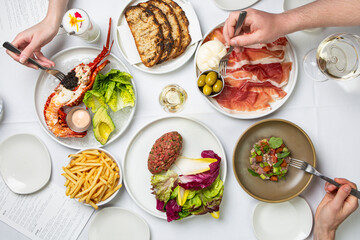 Restaurant flat lay featuring lobster, steak tartare, fries and more.