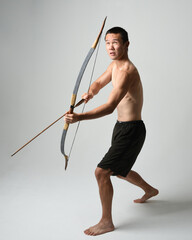 Full length portrait of fit  asian male model,  Holding hunting bow and arrow archery weapon,...