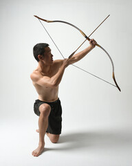Full length portrait of fit  asian male model,  Holding hunting bow and arrow archery weapon,...